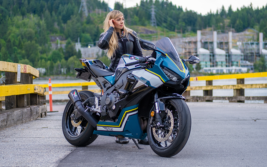 Blond woman standing right behind of a sport motorbike in a road outside the city 