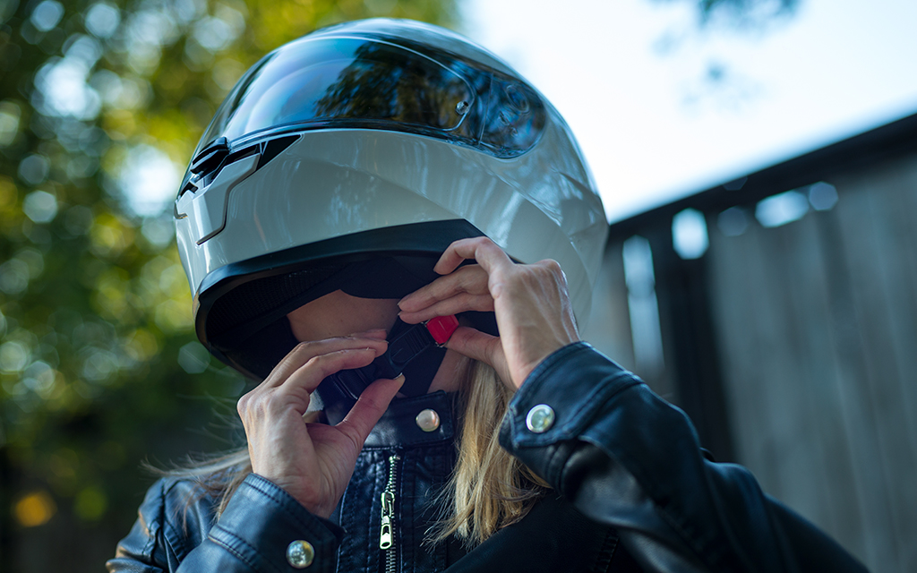 Women wearing a leather jacket fastening her motorcycle white helmet 